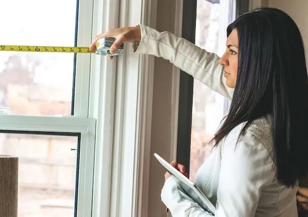 a woman measuring a window with a tape measure